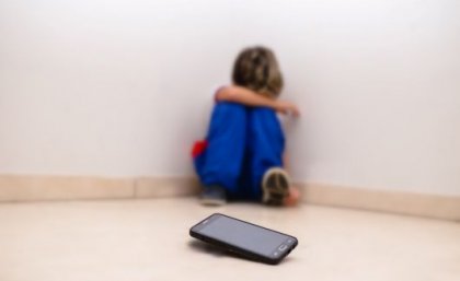 Higher screen use could exacerbate a child's social-emotional problems, in turn driving them to screens as a coping mechanism. Image: Adobe. Upset child sits away from cell phone device